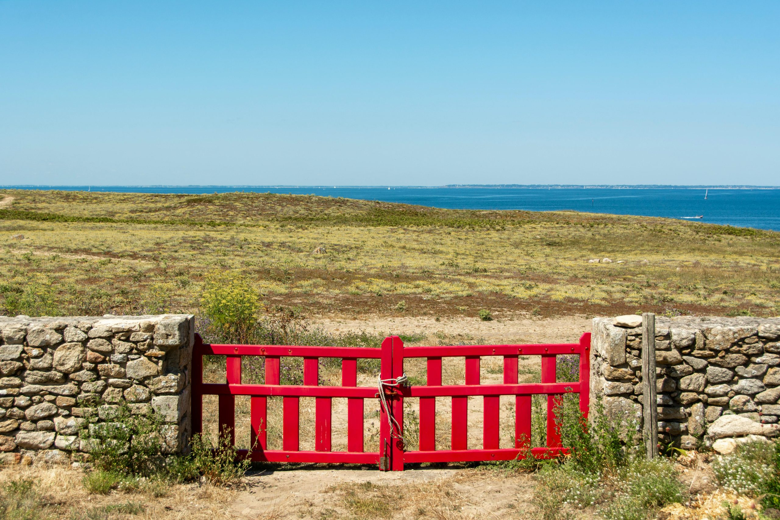 A vibrant red gate set against the beautiful landscape of Hoëdic Island, France.