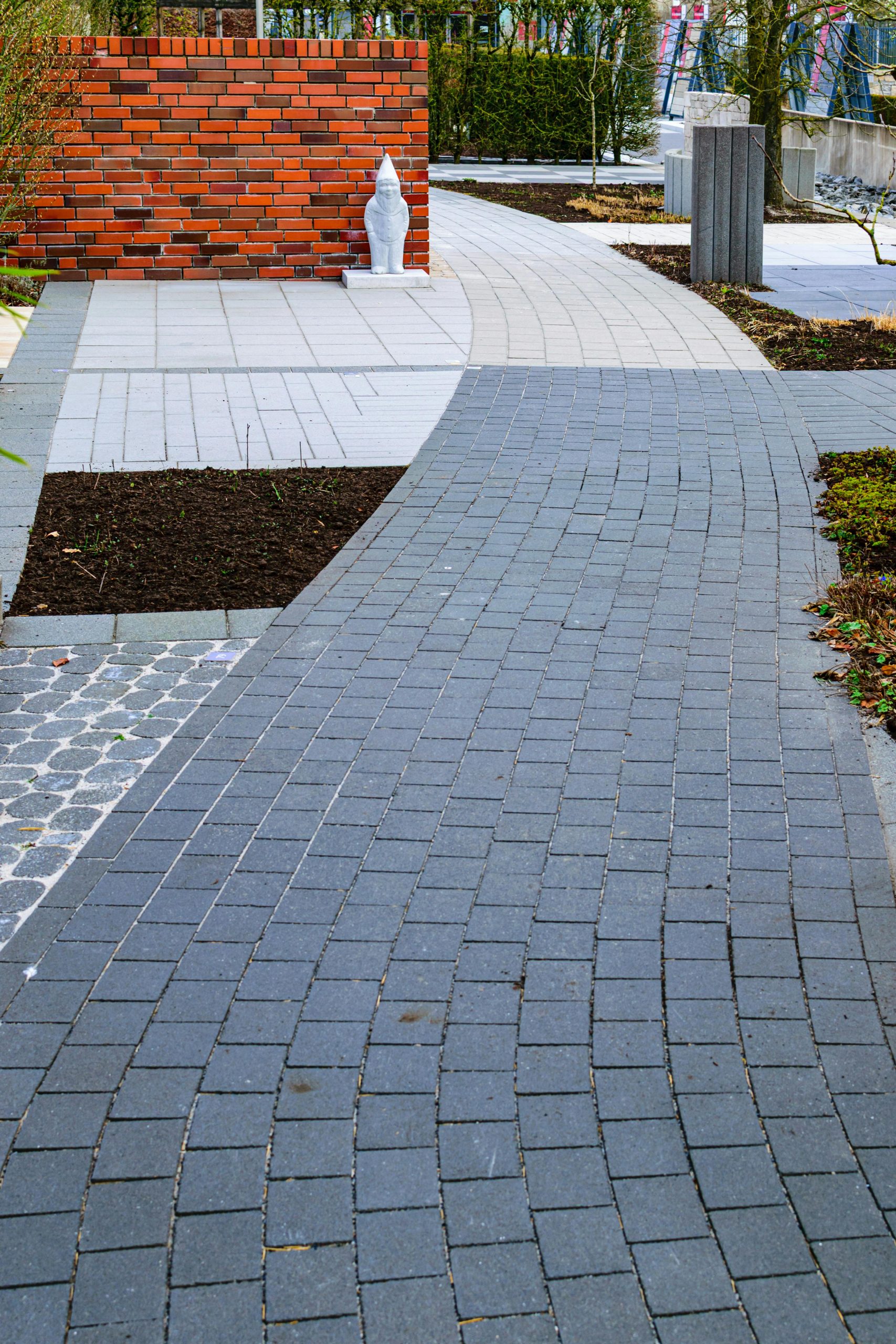 A curved brick pathway in a modern urban garden with red bricks and greenery.